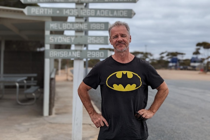 A man with a batman shirt stands with his hands on his hips. 