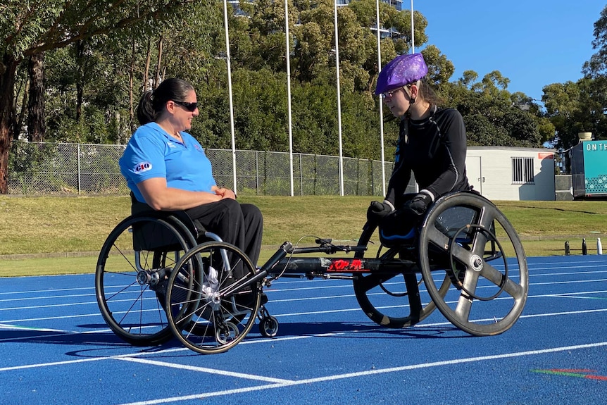 Two wheelchair athletes sit talking together on the track.