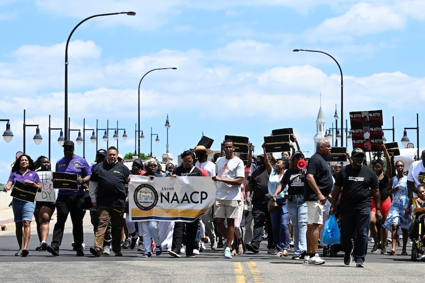 A group of protesters carrying a banner which says "NAACP" 