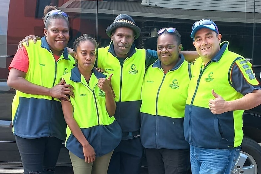 A group of ni-Vanuatu seasonal workers stand together wearing hi-vis jackets