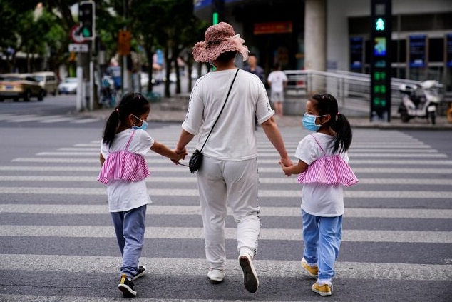 A mother walks with her twin daughters on a street