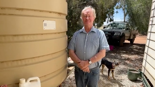 Tim O'Halloran stands next to his water tank with his dog behind him