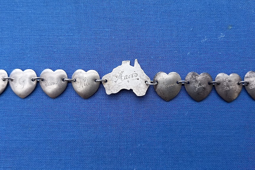 A silver bracelet on a blue background. The bracelet is made up of one link shaped like Australia and eight hearts.