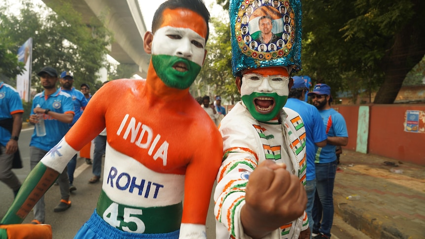 Two Indian fans, whose facies and bodies are covered in orange, green and white paint