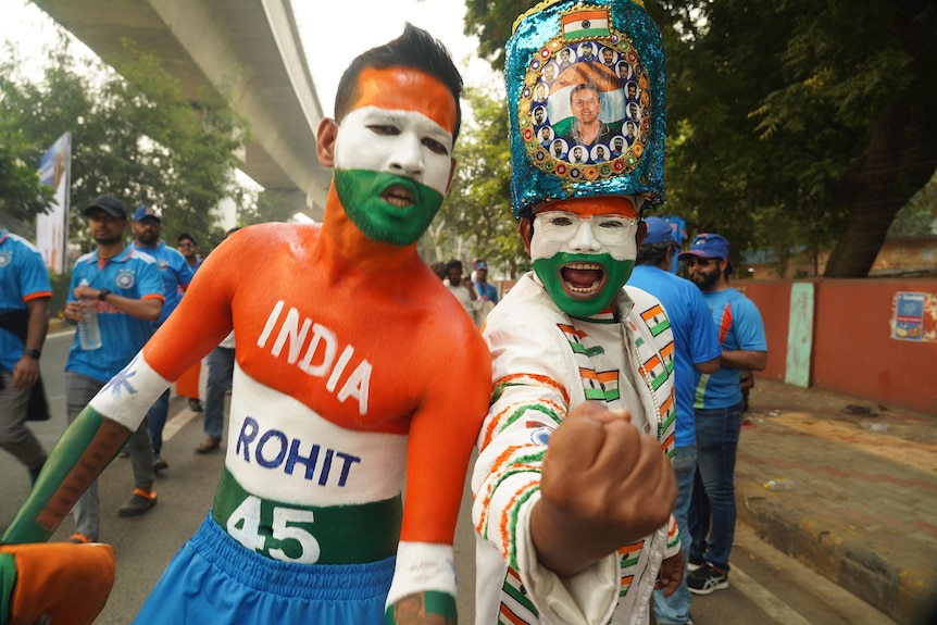 Two Indian fans, whose facies and bodies are covered in orange, green and white paint