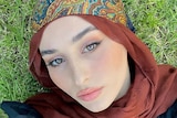 A woman in a brown hijab lying on the grass.