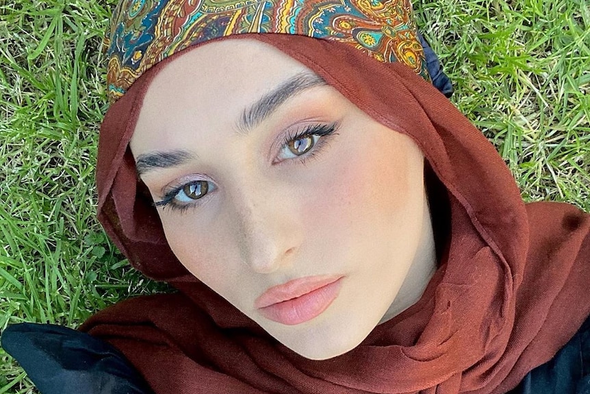 A woman in a brown hijab lying on the grass.