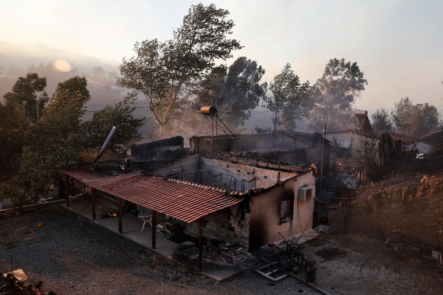 A burned house with the roof missing. Trees and smoke haze in the background. 