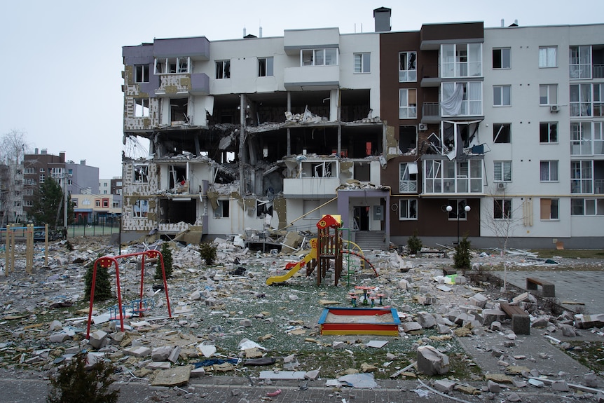 An empty platyground in front of a partially caved-in apartment building with shattered windows