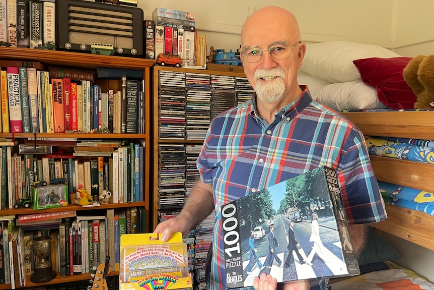 A man smiling holding items from his Beatles collection