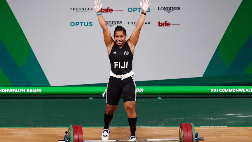 Wide shot of a female weightlifter with her arms raised in celebration.