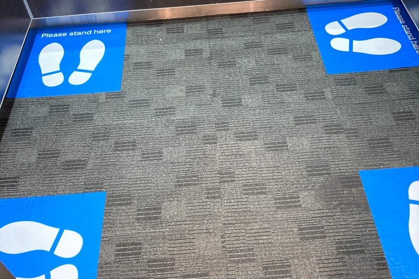 A floor of a lift showing four sets of feet symbols, white on blue in the four corners of the lift.