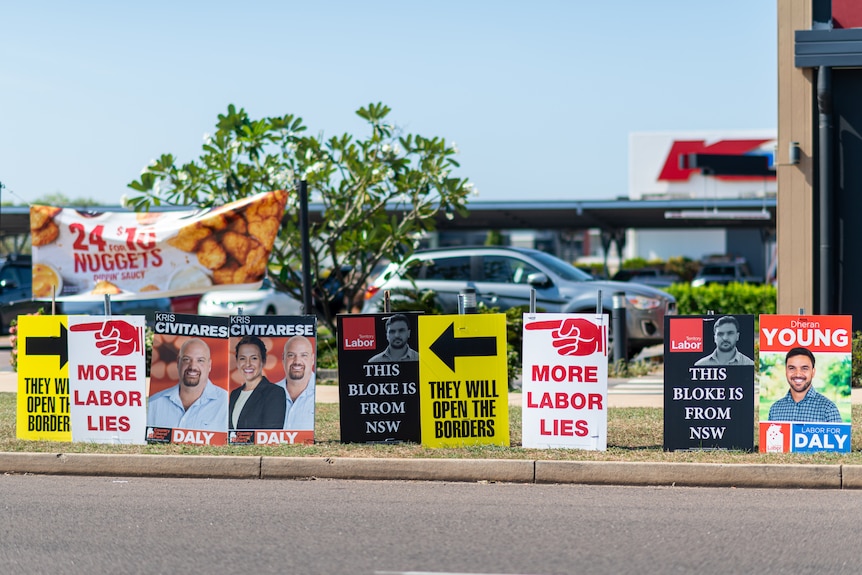 Colourful corflute signs promoting different election candidates on display on the side of a road.