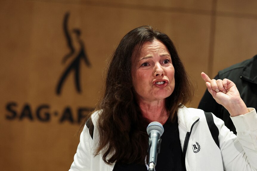 Fran Drescher outrage and pointing a figure in front of SAG AFTRA signage. 