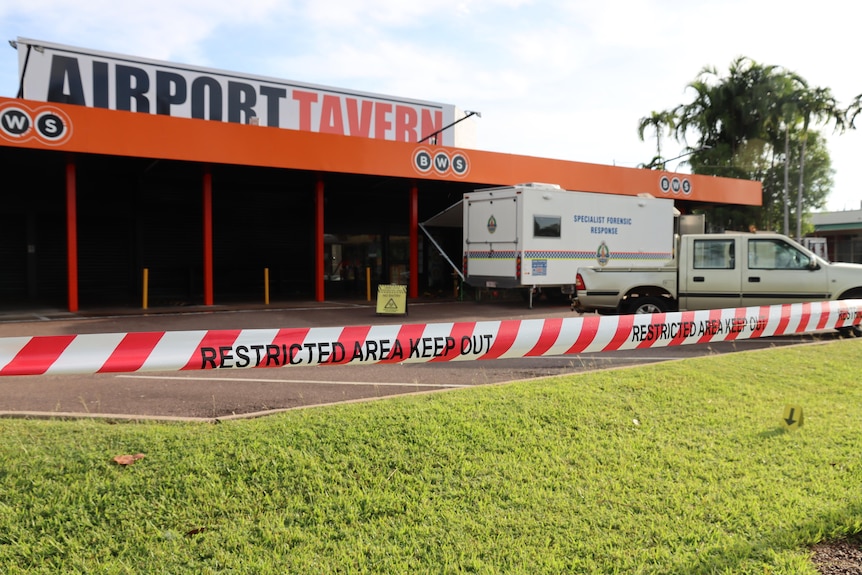 A bottle shop shopfront under a large sign reading 'Airport Taver', with police tape in the foreground.