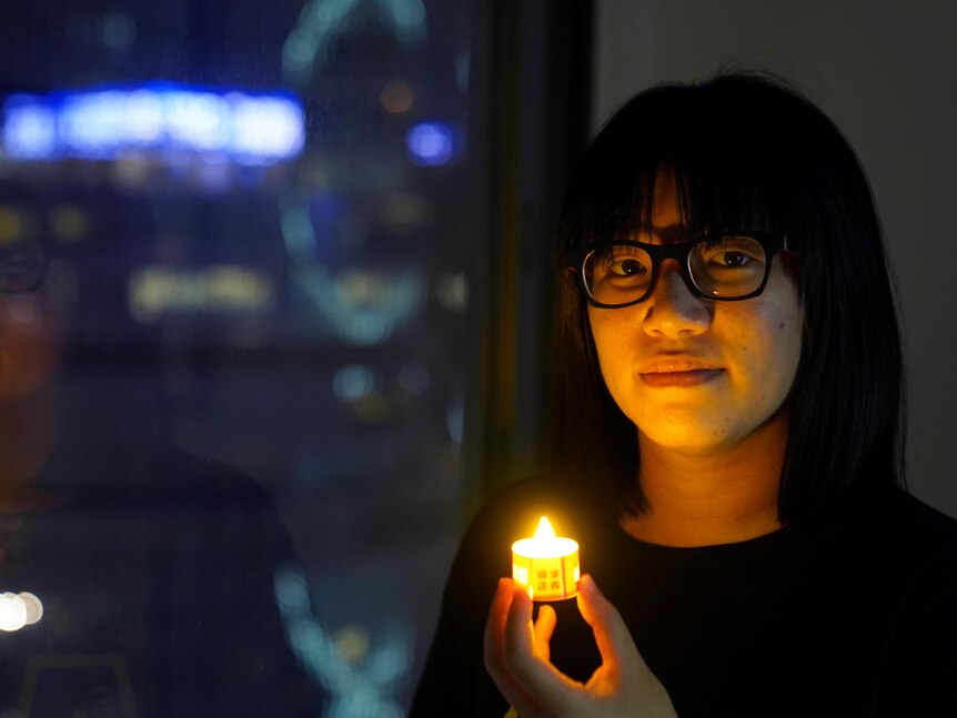 A woman whose face is illuminated by the tea light candle she's holding. 