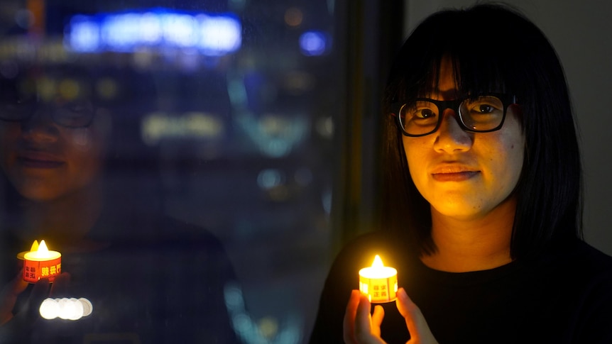 A woman whose face is illuminated by the tea light candle she's holding. 
