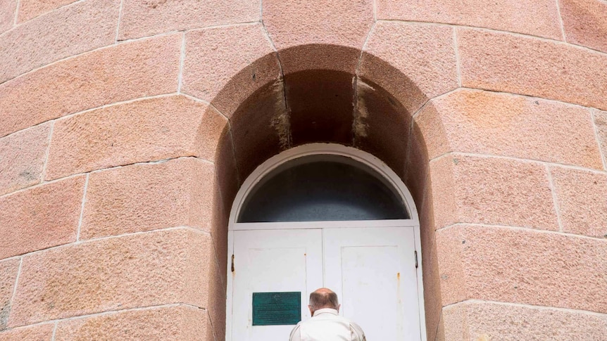 Tony Symes is miniaturized by the tower's mass of pink granite as he locks the doors in an archway.