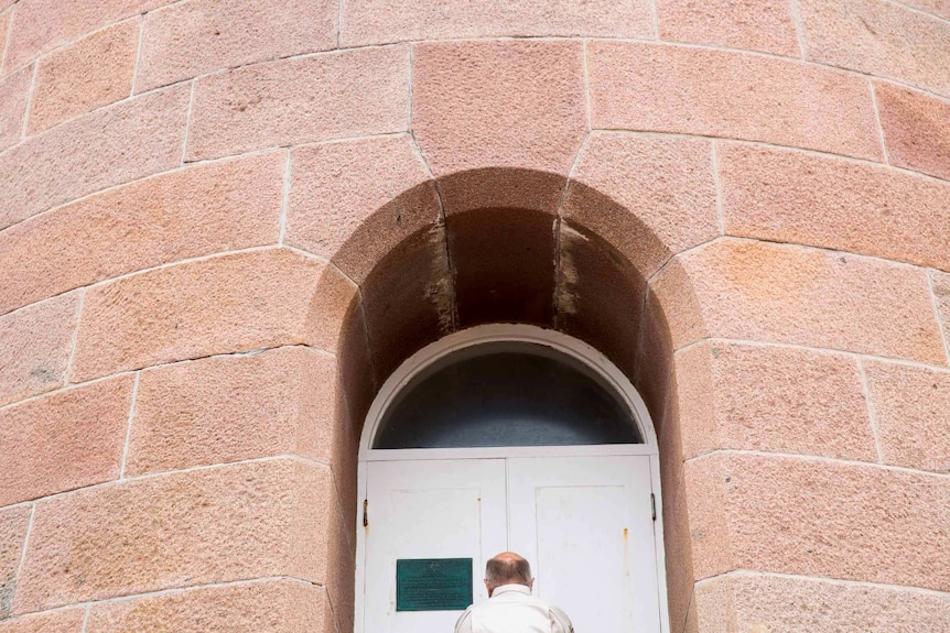 Tony Symes is miniaturized by the tower's mass of pink granite as he locks the doors in an archway.