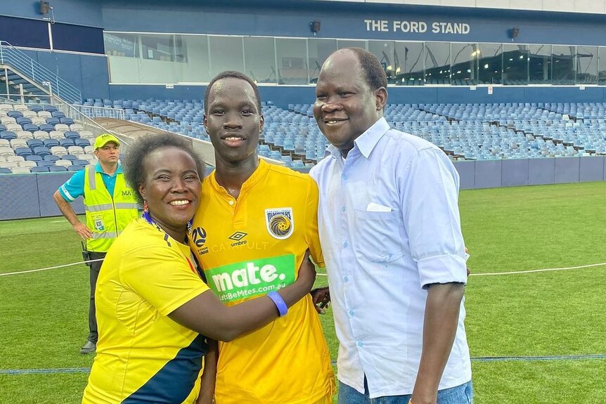 A young man with his parents on a soccer pitch.