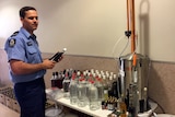 Piolice officer stands near an alcohol still with softdrink bottles of spirits.