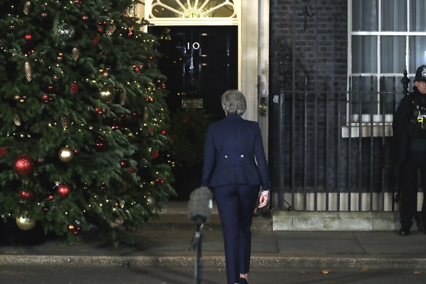 Theresa May walks away from a microphone outside 10 Downing Street, towards the door. There is a large Christmas tree next her.