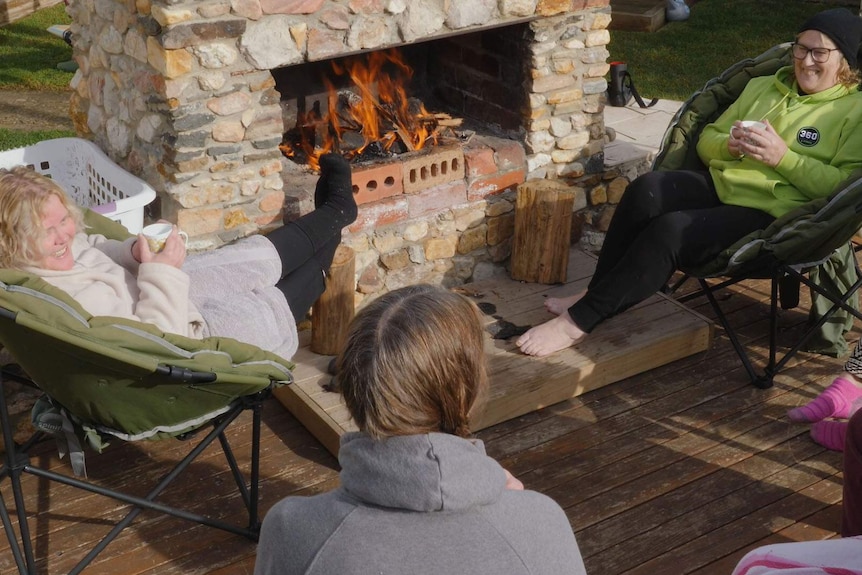 A group of ladies in warm clothing, warming up next to outside fireplace