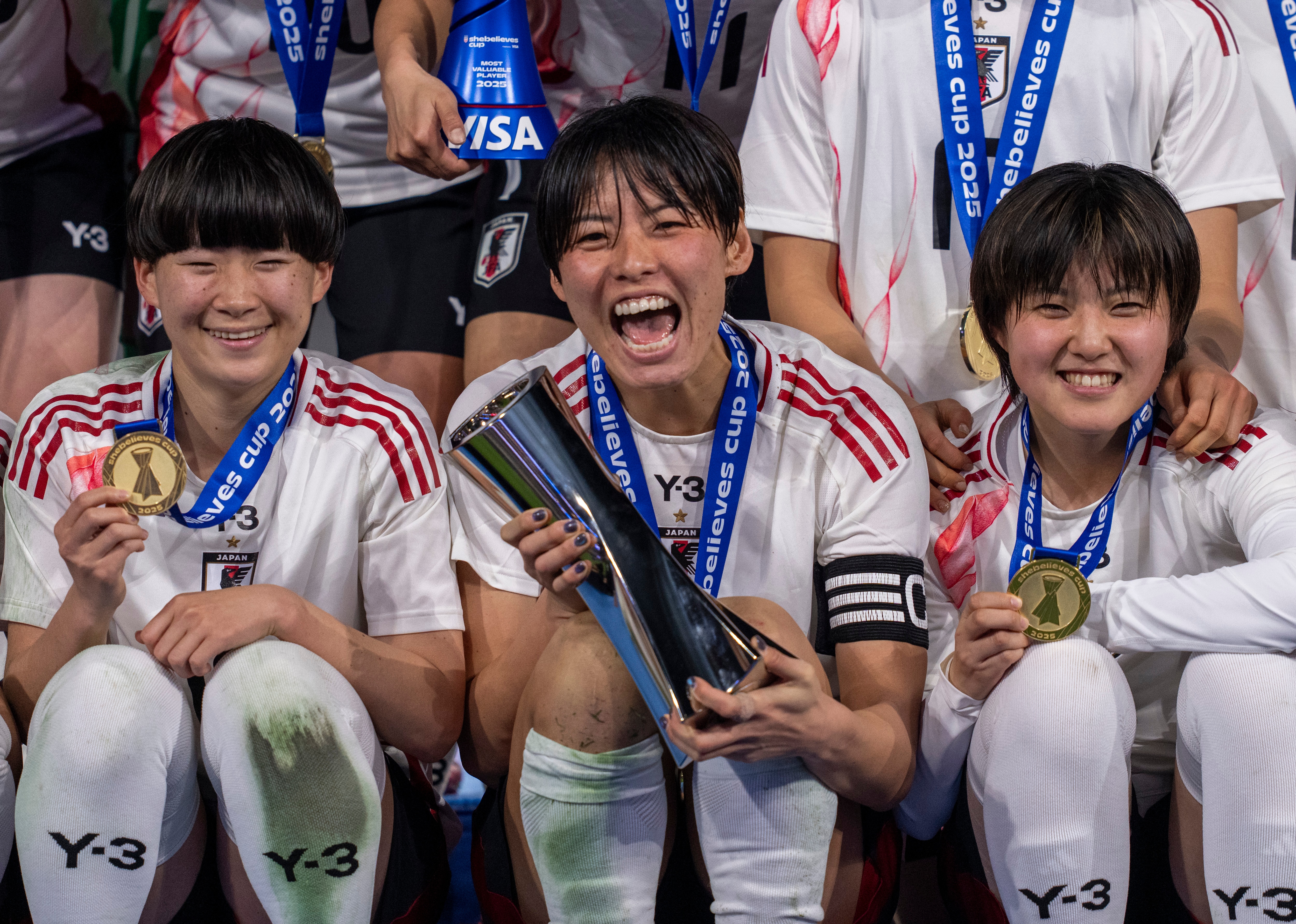 Uma imagem aproximada das jogadoras japonesas, uma jogadora segura o troféu SheBelieves e sorri.