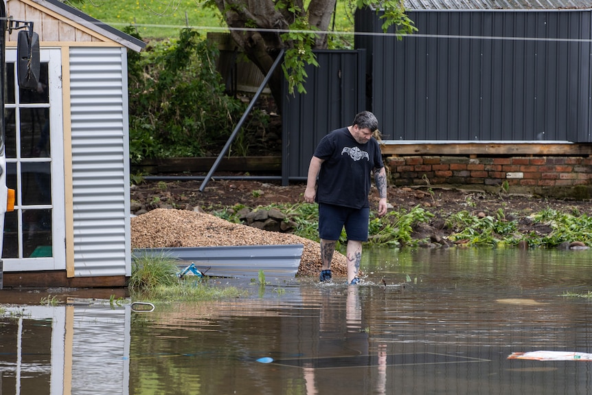 A man wades through floodwater looking down. 