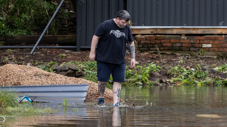A man wades through floodwater looking down. 