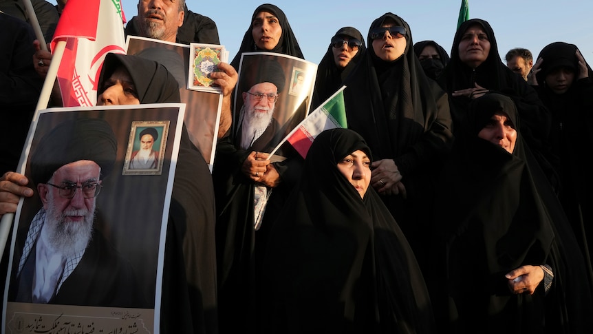 Women covered in black abiyas hold posters of the Supreme Leader Ayatollah Ali Khamenei.
