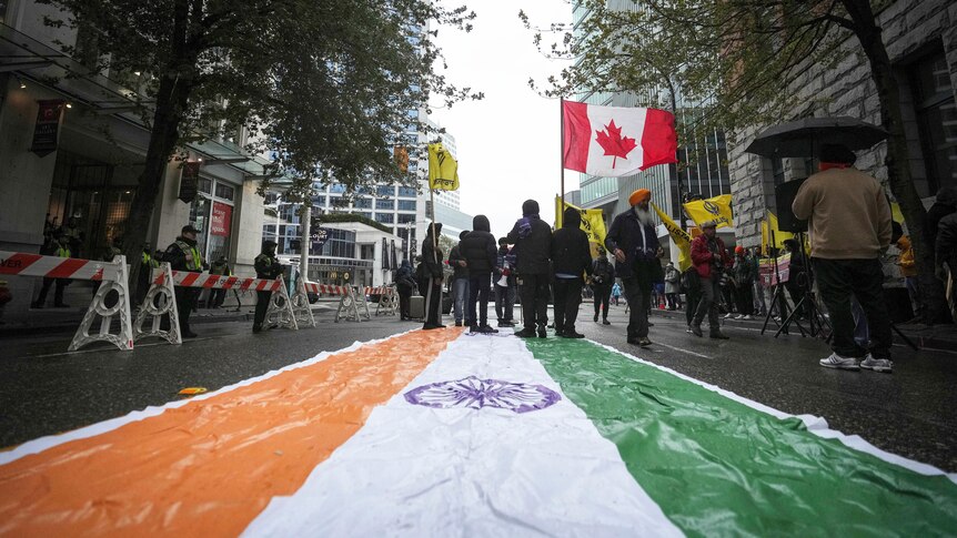 An Indian flag is laid on a street as protesters wave the flags of Canadian and Khalistan.