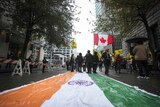 An Indian flag is laid on a street as protesters wave the flags of Canadian and Khalistan.