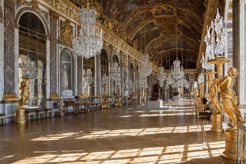A large hall filled with crystal chandeliers, gold statues, artworks and mirrors.