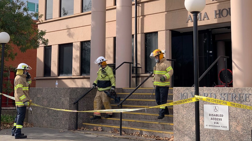 Firefighters walk down the steps of a modern building with crime scene tape around