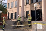 Firefighters walk down the steps of a modern building with crime scene tape around