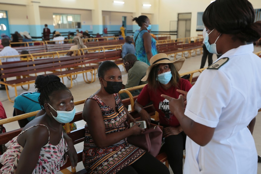 A nurse speaks with three women in masks.