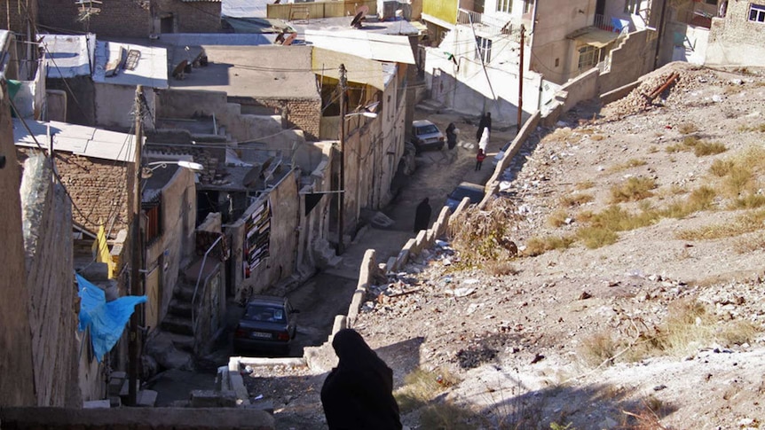 A veiled woman walks down a path into slums