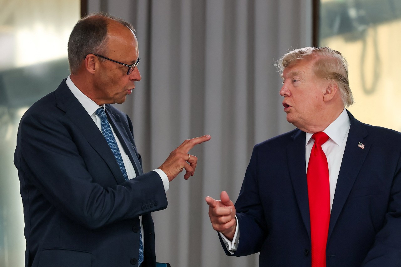 Two men in suits, speaking and pointing. 