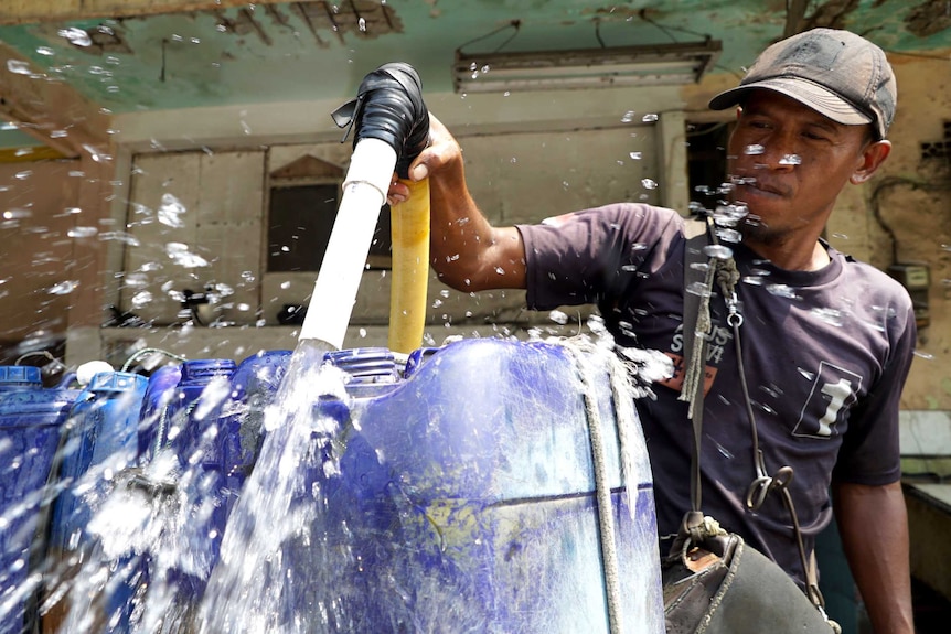 A water vendor uses a hose to fill his containers with fresh water.