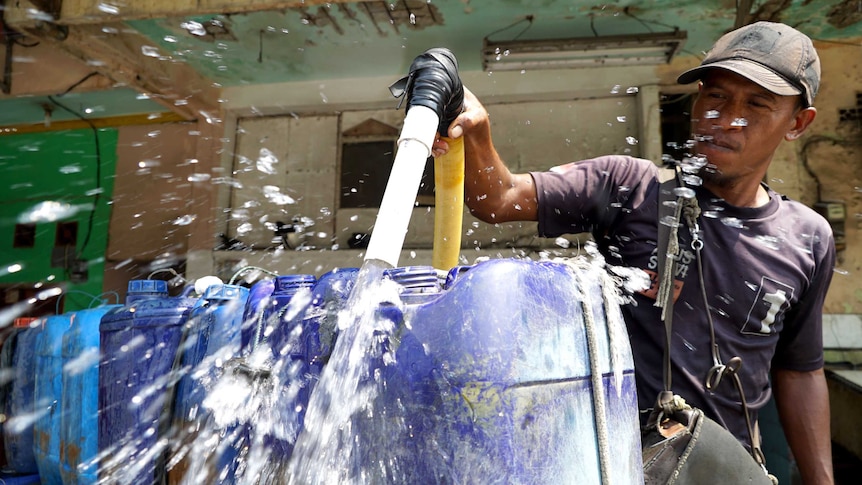 A water vendor uses a hose to fill his containers with fresh water.