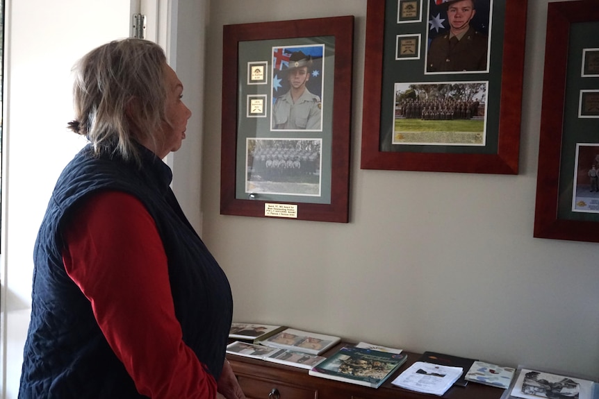 Sandra is wearing a red top and looking at the photo frames of her grandsons mounted on the walls