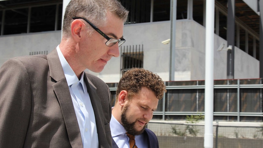 Dimitrios Brendas walks away from the ACT Magistrates Court wearing a brown suit and glasses, alongside his lawyer.