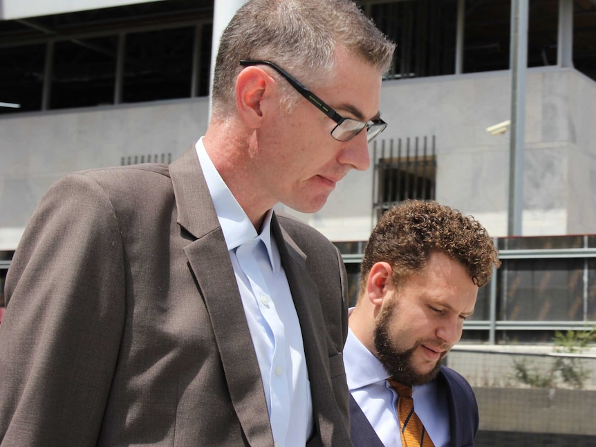 Dimitrios Brendas walks away from the ACT Magistrates Court wearing a brown suit and glasses, alongside his lawyer.