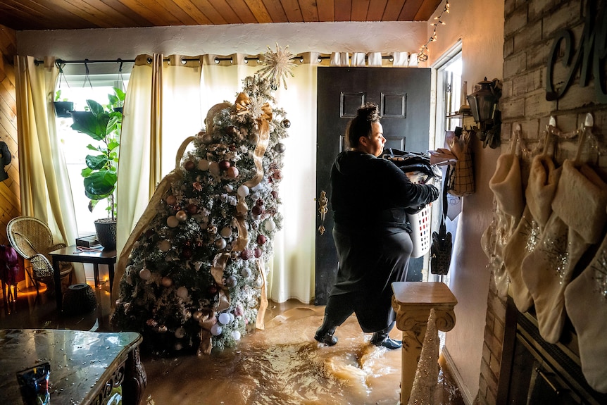 A woman leaving a flooded house with a christmas tree tipped over