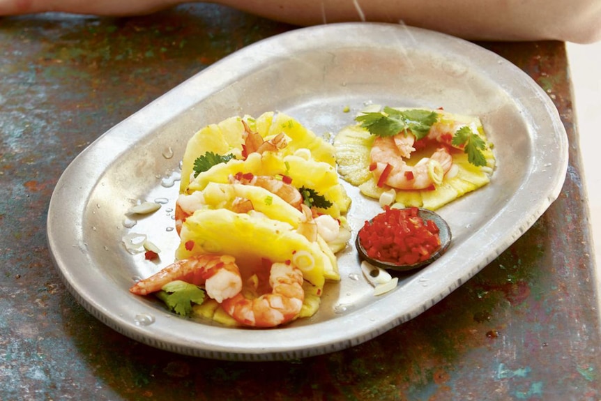 A man squeezes lime over tacos made out of slices of pineapple stuffed with prawns and vegetables