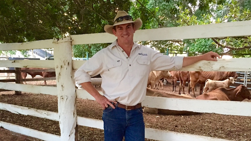 A man in jeans and an akubra standing next to a white cattle yard rail.