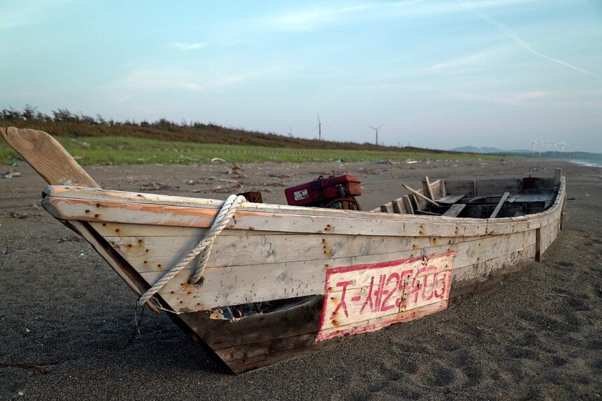 An abandoned wooden boat in poor condition on a beach.