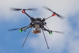 A close-up of a small drone as it flies in mid-air, its rotors are blurry as they spin
