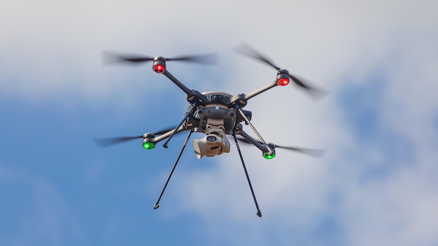 A close-up of a small drone as it flies in mid-air, its rotors are blurry as they spin